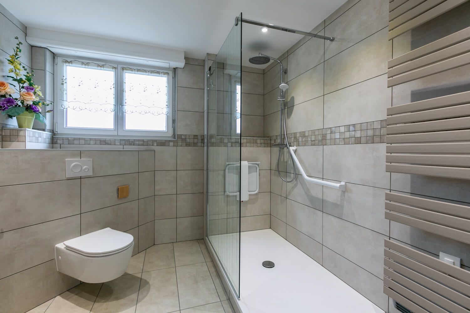 Douche de plain-pied avec barre d'appui et WC suspendu dans une salle de bain rénovée